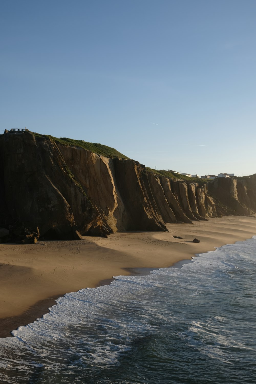 a sandy beach next to the ocean with a cliff in the background