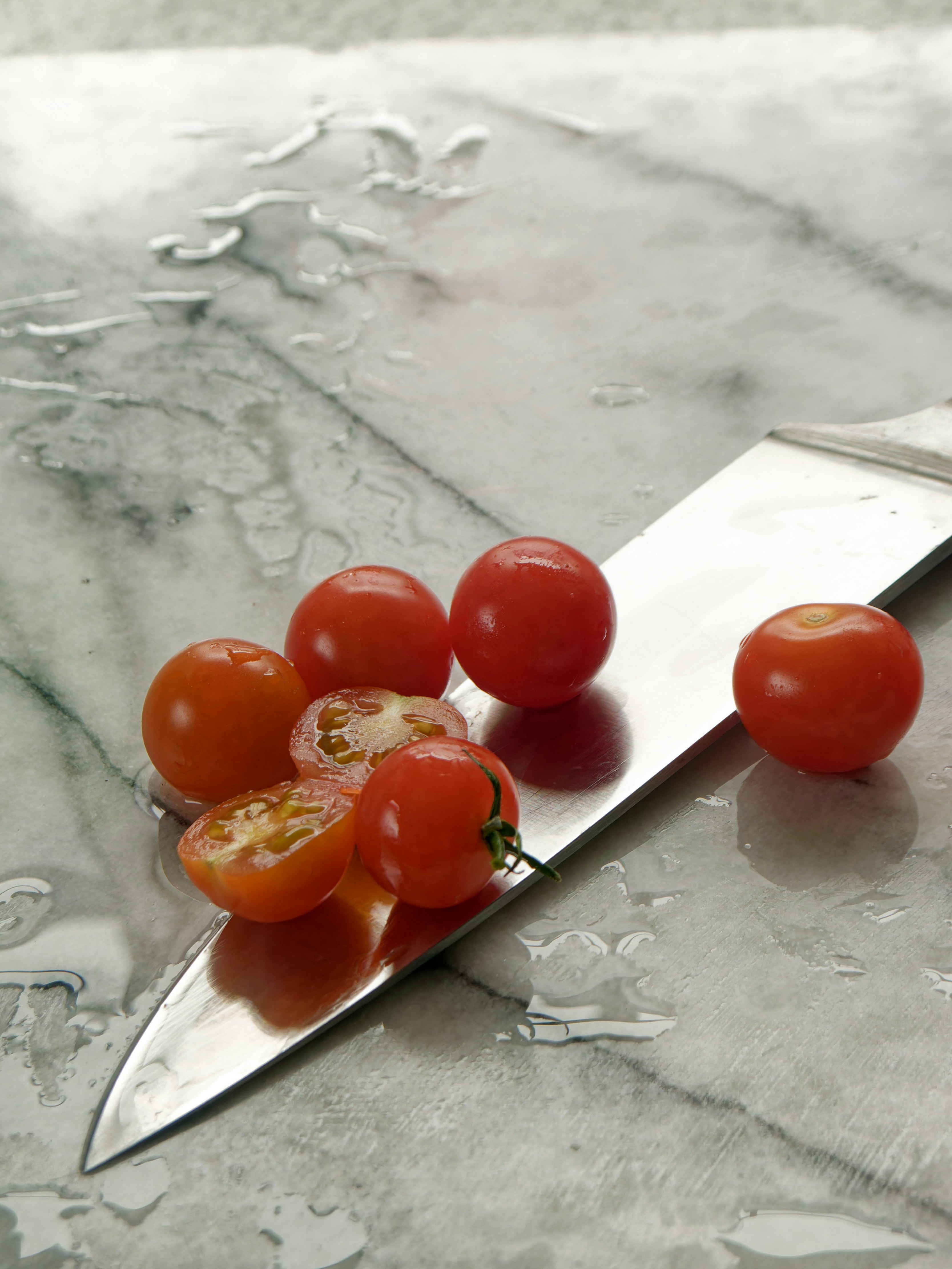 A knife beside cherry tomatoes on a marble counter