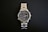 A stainless steel wristwatch with a complex dial featuring multiple sub-dials and a date function, set against a black background. The watch has a polished metal strap and a well-illuminated face highlighting intricate details.