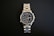 A stainless steel wristwatch with a complex dial featuring multiple sub-dials and a date function, set against a black background. The watch has a polished metal strap and a well-illuminated face highlighting intricate details.
