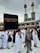 A crowd of people performing the Tawaf, a religious ritual, around the Kaaba in Mecca. The atmosphere is busy and reverent, with men and women dressed predominantly in white robes.