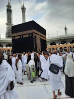 Group photo of happy pilgrims in white Ihram attire near the Kaaba