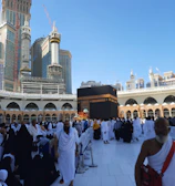 Wide shot of pilgrims performing tawaf around the Kaaba under a clear sky.