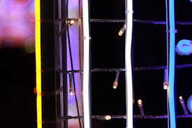 Brightly colored neon lights intertwined with wires against a dark background, featuring prominent orange, white, and blue hues.