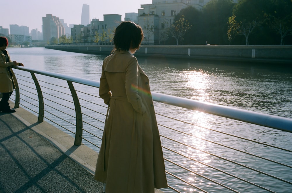 a woman in a trench coat looking out over a river