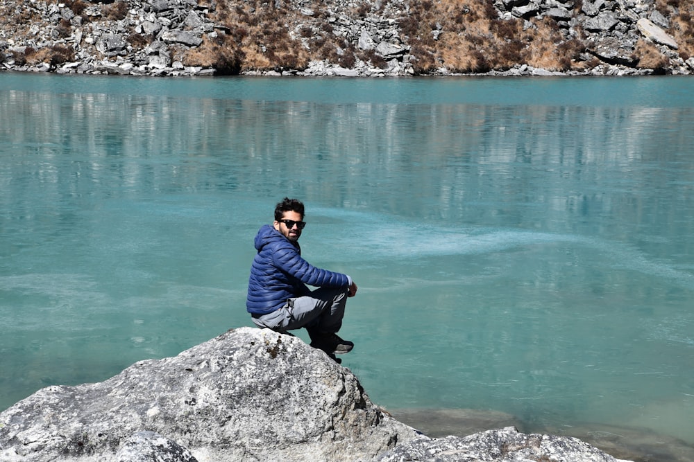 a man sitting on top of a rock next to a body of water