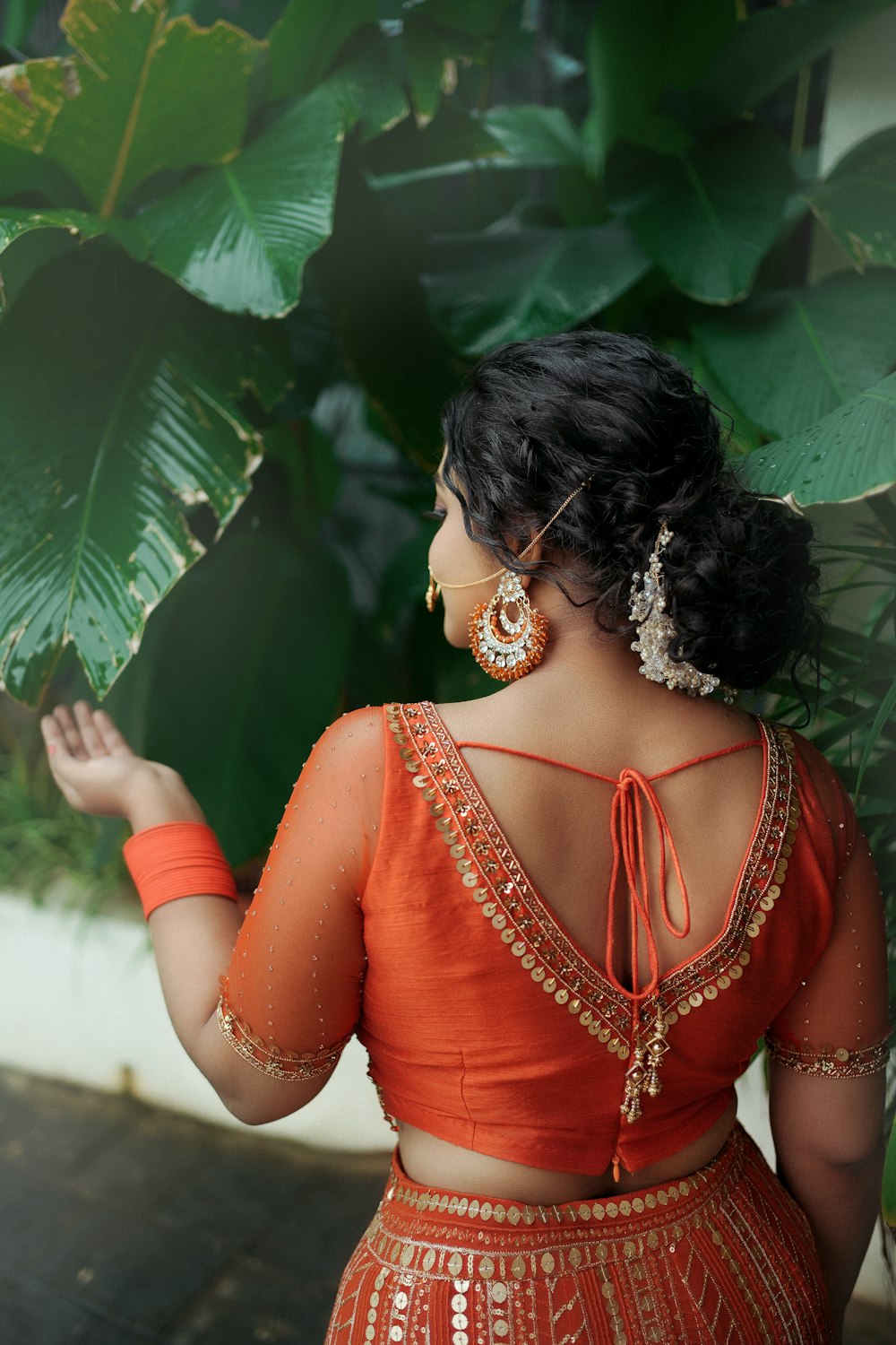 a woman in an orange lehenga standing in front of a plant