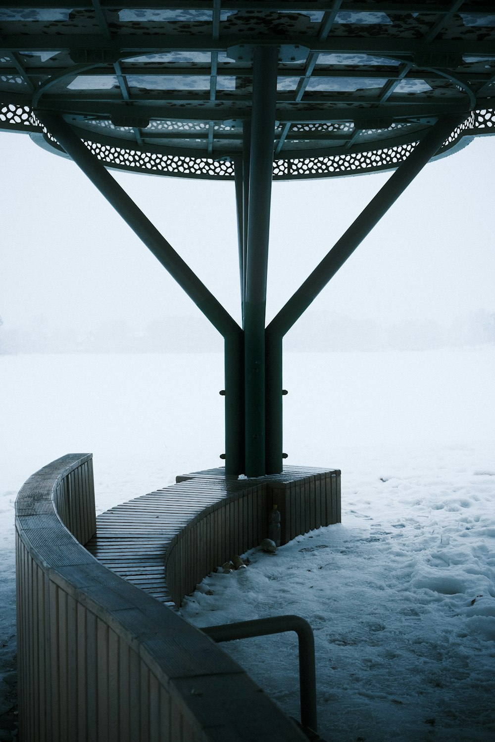 a bench sitting under a metal structure covered in snow