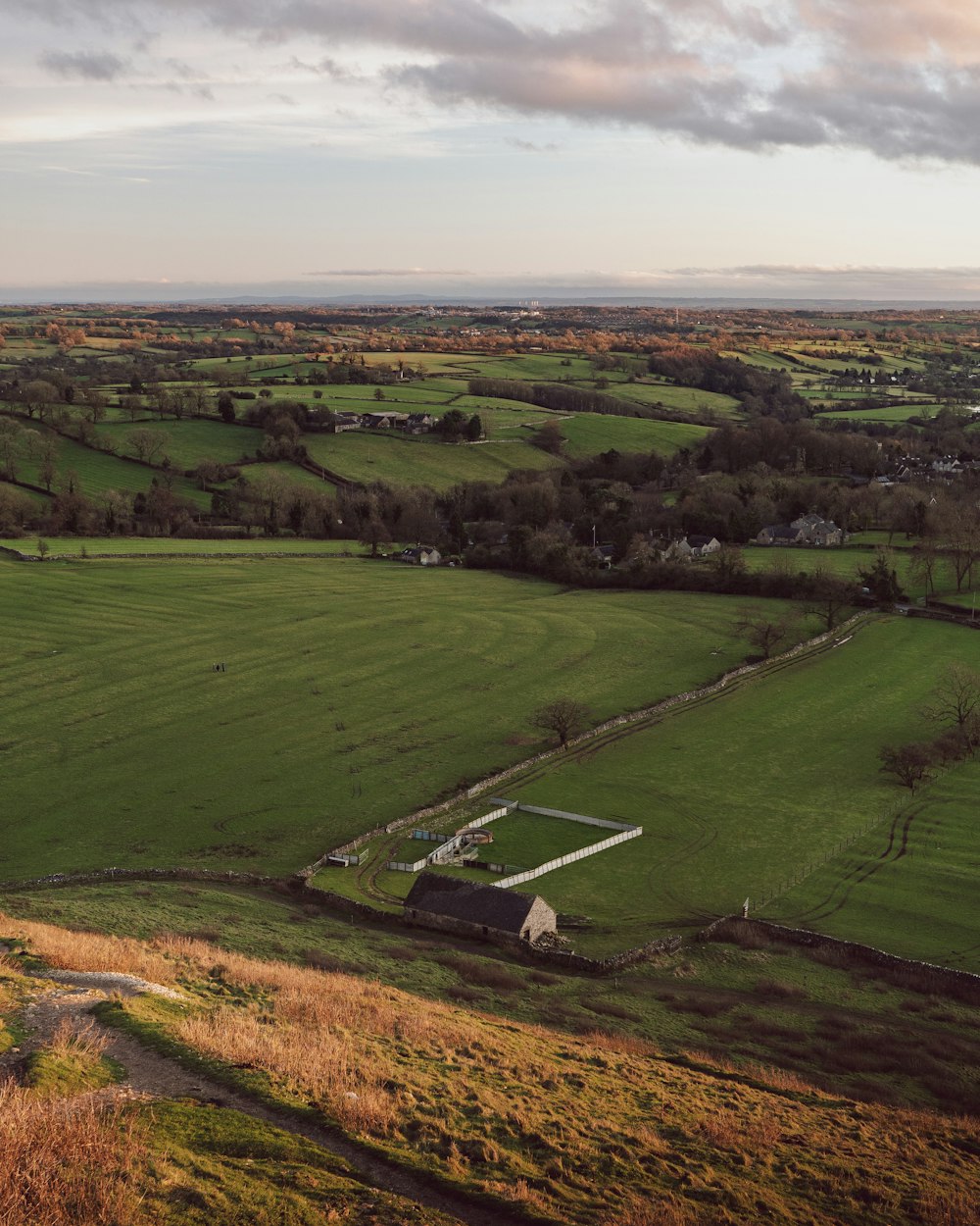 an aerial view of a green field with a barn in the distance