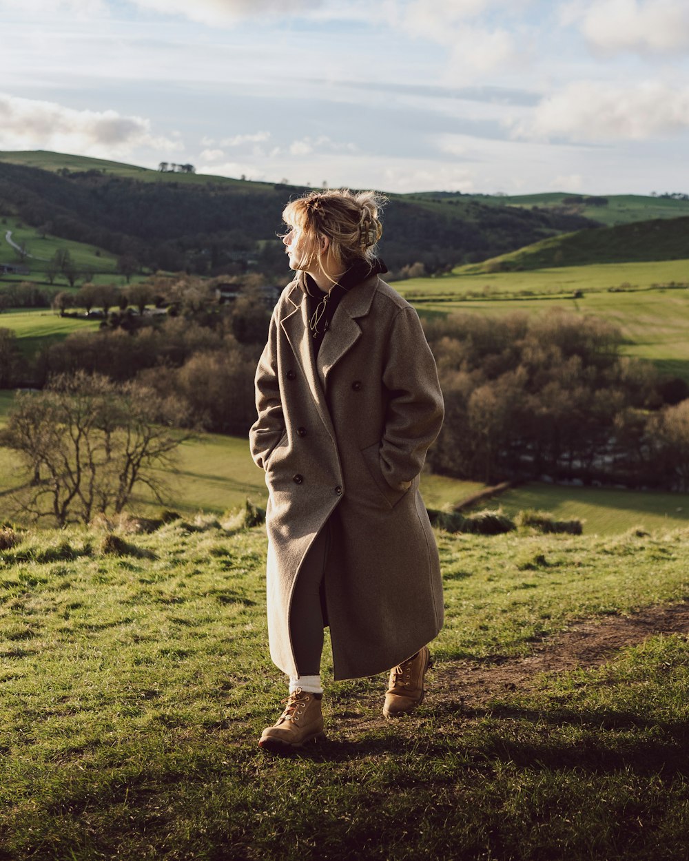 a woman in a trench coat standing on a hill