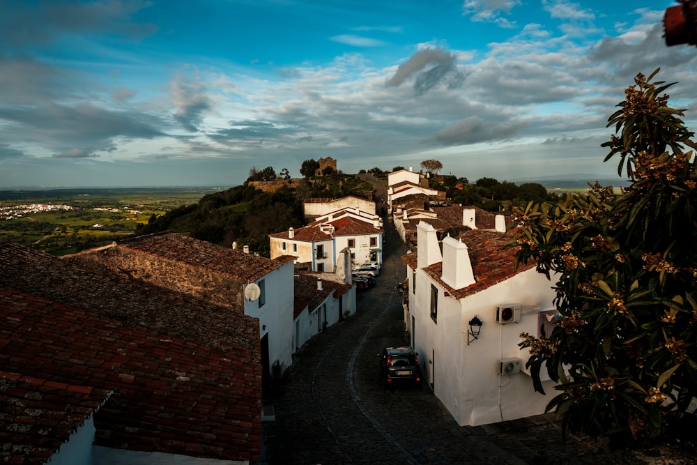 a street lined with white buildings next to a lush green hillside