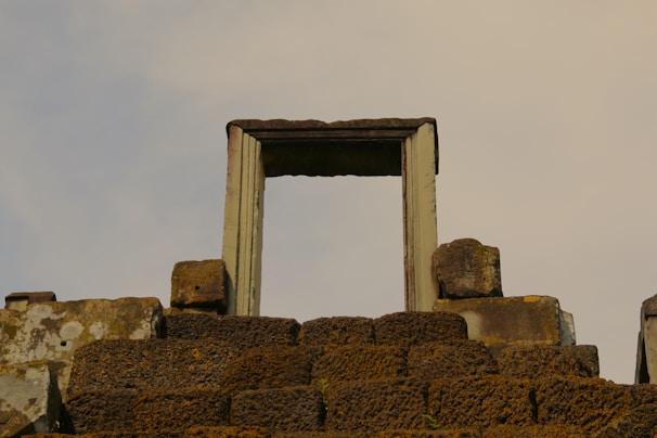 A historic stone structure features an ancient doorway without a door, surrounded by weathered stone blocks. The stones appear aged and moss-covered, giving the scene an ancient and mysterious atmosphere.