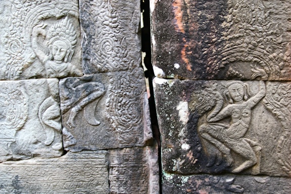 Ancient stone carvings display intricate, detailed figures with elaborate headdresses and traditional poses, set within textured surfaces that showcase artistic skill and cultural significance.