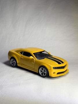 A shiny yellow die cast car on a sunburst yellow display stand with smooth curves.