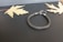 A woven metallic bracelet with a clasp is placed on a dark background. Two dried, pale yellow maple leaves are laid symmetrically on each side of the bracelet, enhancing the contrast between the elements.