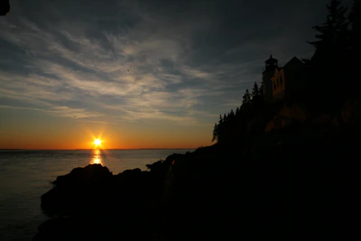 A navy blue and gold lighthouse shining over calm ocean waves at sunset.