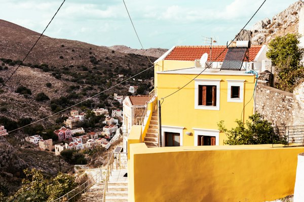 A yellow building with a red roof next to a hillside — Symi, Greece