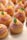 A selection of small, round pastries decorated with sugar, topped with segments of orange and fresh mint leaves. The pastries have a golden-brown color and are arranged neatly on a light-colored surface.