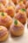 A selection of small, round pastries decorated with sugar, topped with segments of orange and fresh mint leaves. The pastries have a golden-brown color and are arranged neatly on a light-colored surface.