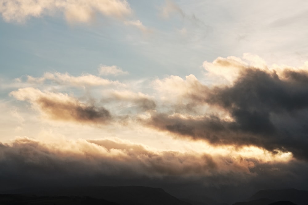 a plane flying through a cloudy sky with mountains in the background