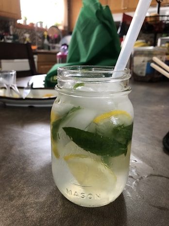 A refreshing mint and cucumber infused water jar with slices of lemon and a peach cloth underneath.