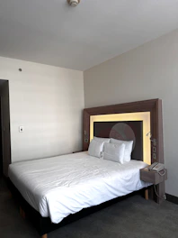 Simple, neat bed with crisp white sheets and a small bedside lamp in Senai.