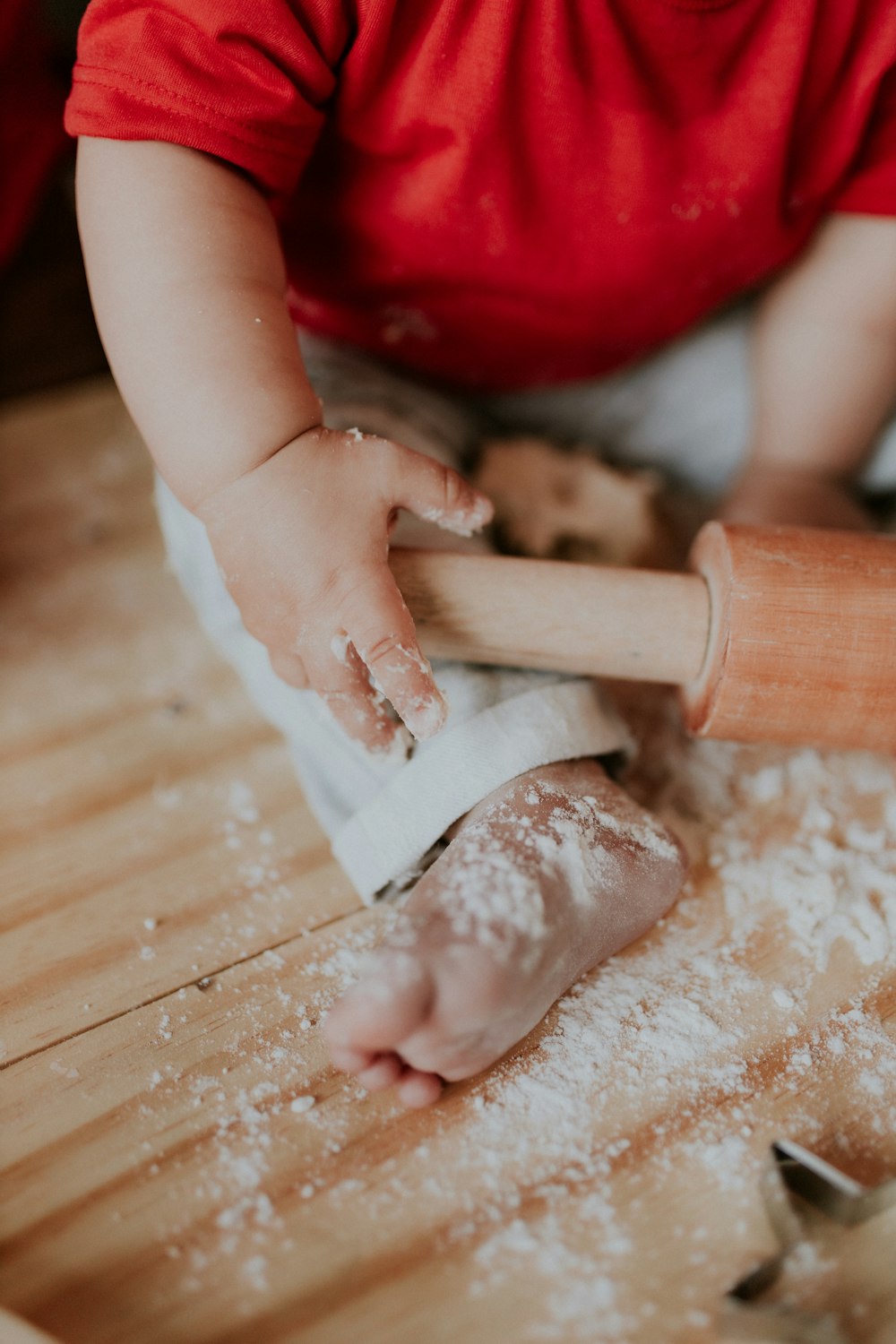 a child rolling dough on top of a wooden table