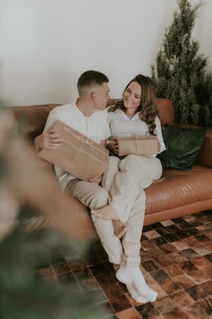A smiling couple enjoying a gift basket filled with fruits, wine, and personalized items in a warmly lit living room.