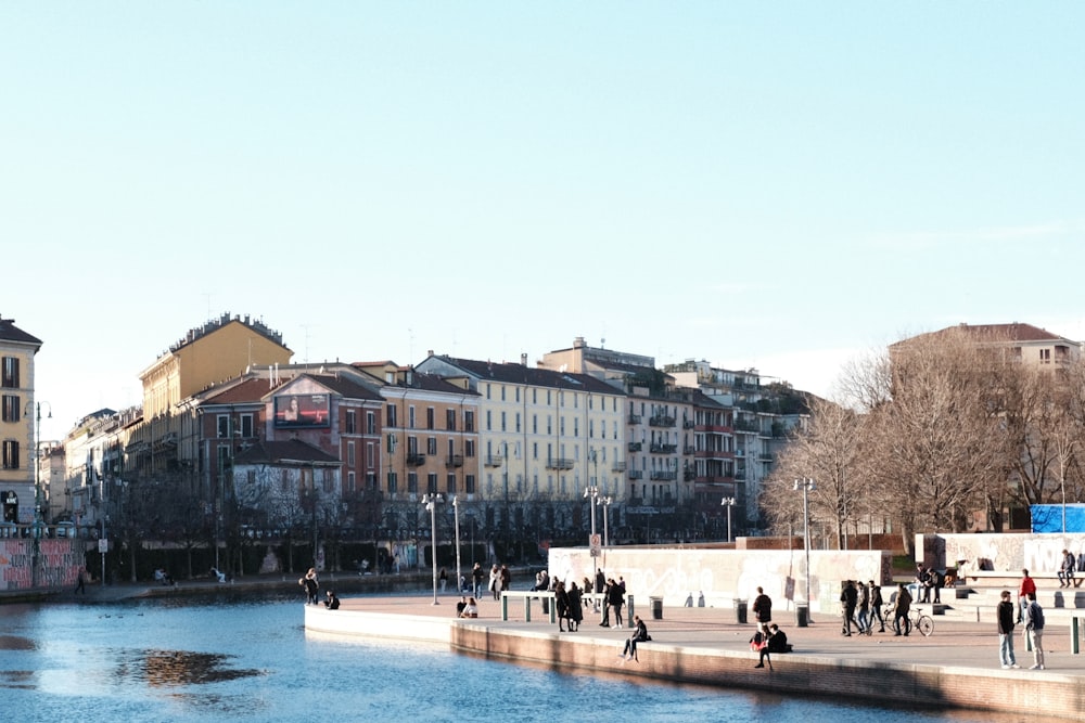 a group of people walking along a river next to tall buildings