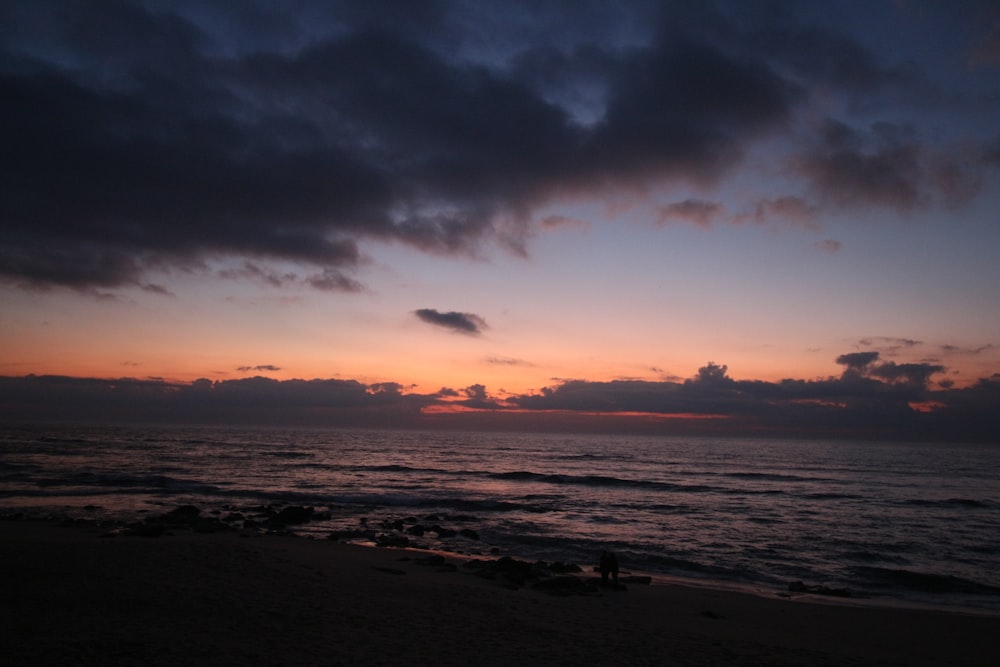 the sun is setting over the ocean on a cloudy day