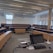 A modern lecture hall or classroom featuring tiered seating with wooden desks and blue cushioned seats. At the front, there is a lectern equipped with a monitor, a control panel, and various stationery items. The room is well-lit by natural light coming through large windows along the right side of the room. Ceiling-mounted projectors and speakers are also visible.