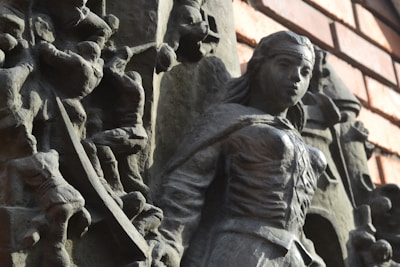A detailed stone relief sculpture featuring a central figure that appears to be a majestic and powerful character, possibly depicting an angel or a warrior, with detailed armor and flowing garments. Surrounding this central figure are other carved figures, creating a dynamic and intricate composition.