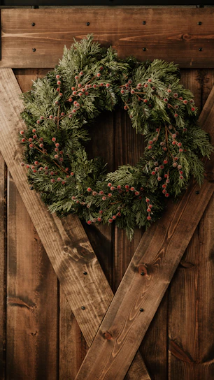 A close-up of a vibrant custom wreath featuring lush greenery and delicate flowers on a rustic wooden door.