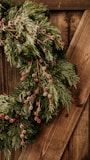 A festive wreath made from natural, recycled materials with vibrant red and green accents.