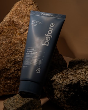 A tube of 'before' purifying toothpaste rests against a backdrop of textured rocks. The toothpaste tube is blue with white text advertising a super mint whitening formula.