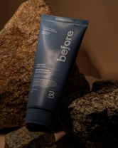 A tube of 'before' purifying toothpaste rests against a backdrop of textured rocks. The toothpaste tube is blue with white text advertising a super mint whitening formula.