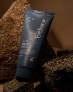 A tube of 'before' purifying toothpaste rests against a backdrop of textured rocks. The toothpaste tube is blue with white text advertising a super mint whitening formula.