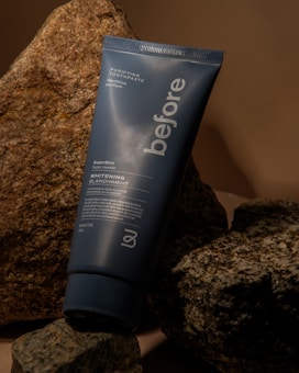 A tube of 'before' purifying toothpaste rests against a backdrop of textured rocks. The toothpaste tube is blue with white text advertising a super mint whitening formula.