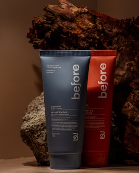 Two toothpaste tubes are positioned against a backdrop of textured, bark-like material. The tube in the foreground is blue and prominently displays the brand name 'before' and the text 'Whitening.' The tube behind it is red with similar branding.
