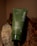A green tube of 'before' purifying toothpaste labeled SuperMint, placed against a background of rocks and wood. The tube is vertically oriented, partially leaning on the textured surfaces.
