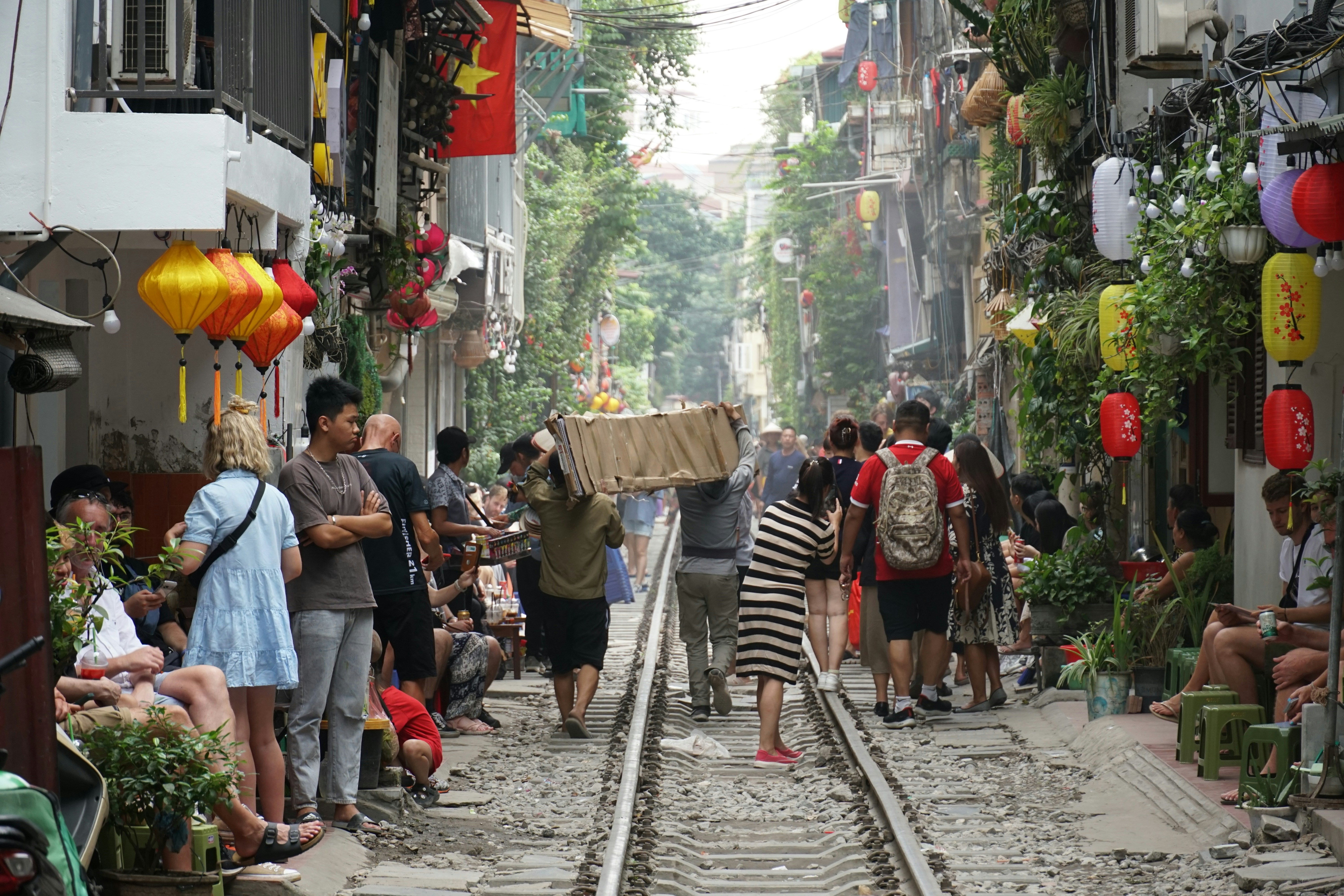 a group of people walking down a street next to a train track, Train street, Hanoi, Vietnam