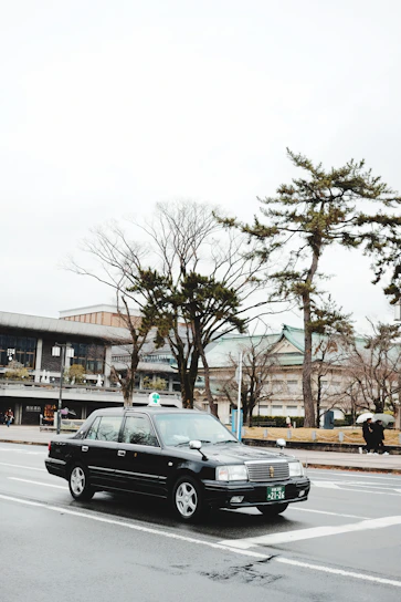 A sleek black taxi parked outside Leeds train station on a rainy day.