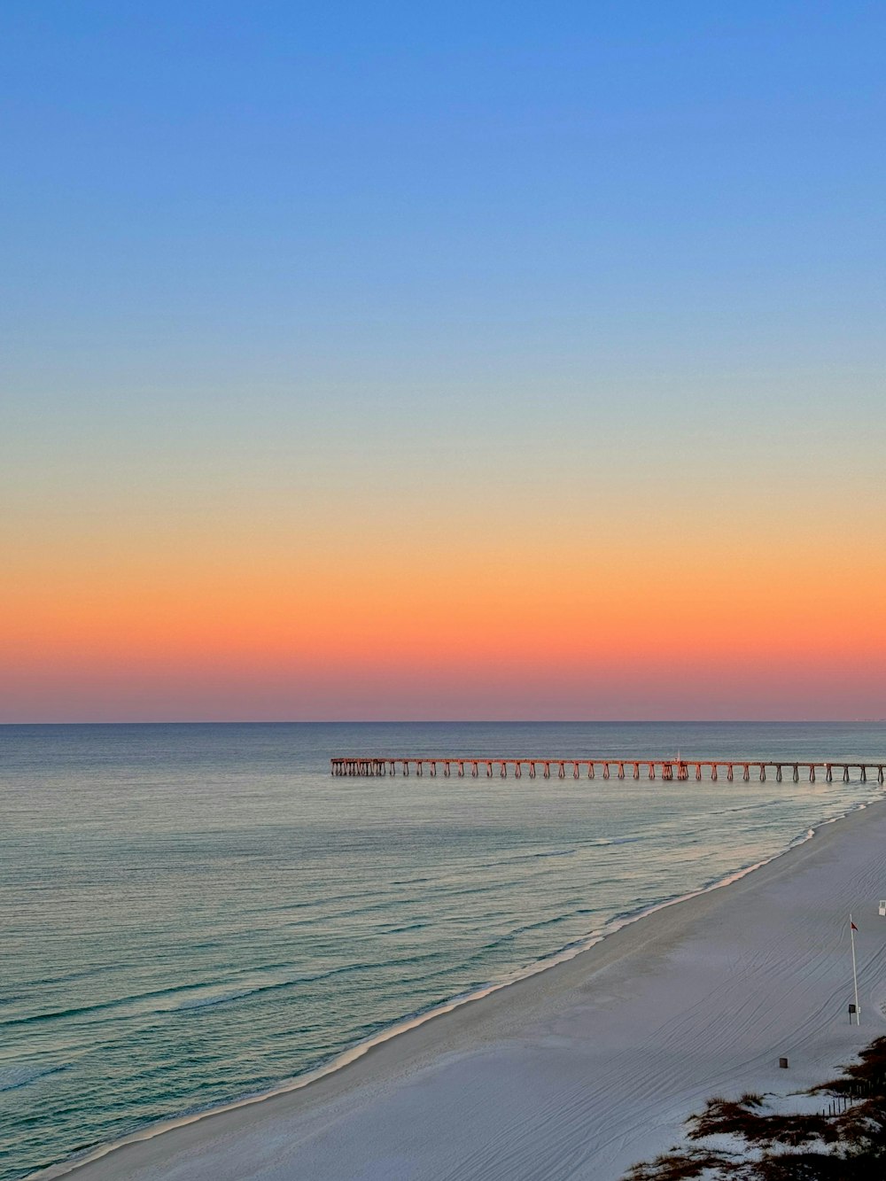 a view of a beach at sunset with a pier in the distance