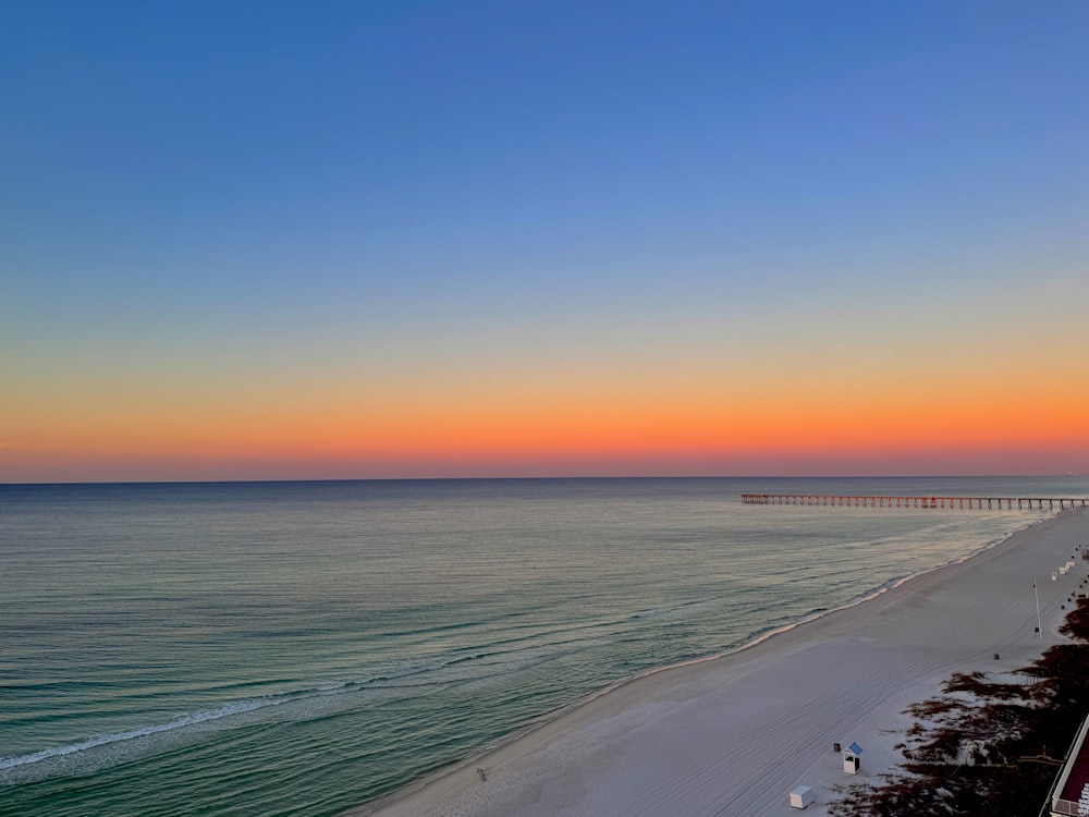 a view of a beach at sunset with a pier in the distance