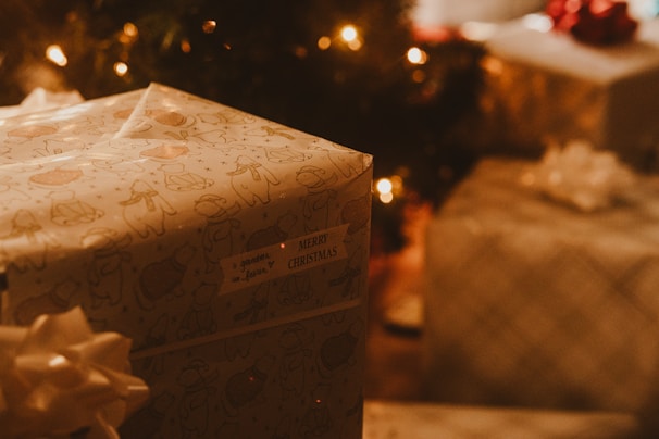 A beautifully wrapped Christmas gift box with festive red and gold ribbons, surrounded by twinkling fairy lights.