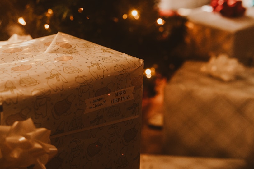 A beautifully wrapped Christmas gift box with a red ribbon, set against a softly lit festive background.