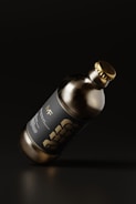 A dark glass bottle with a metallic cap is tilted against a dark background. The label on the bottle features bold typography with the word 'BEER'. The overall aesthetics of the image suggest minimalistic and modern design with an emphasis on sleekness.