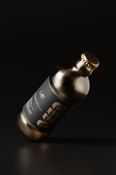 A dark glass bottle with a metallic cap is tilted against a dark background. The label on the bottle features bold typography with the word 'BEER'. The overall aesthetics of the image suggest minimalistic and modern design with an emphasis on sleekness.