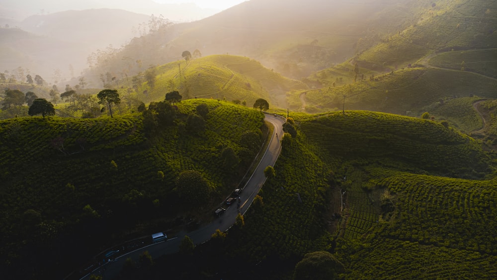 a car driving down a winding road in the middle of a lush green hillside