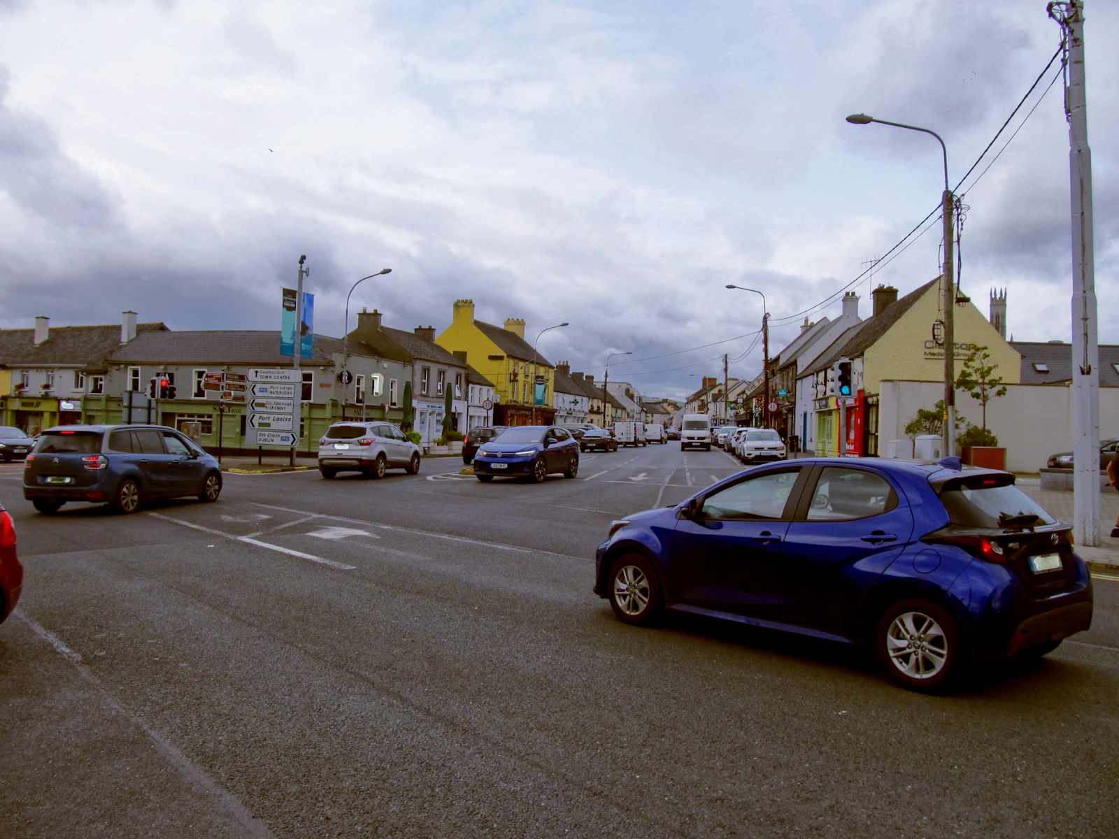 Blue rental car moving along a street in an Irish town